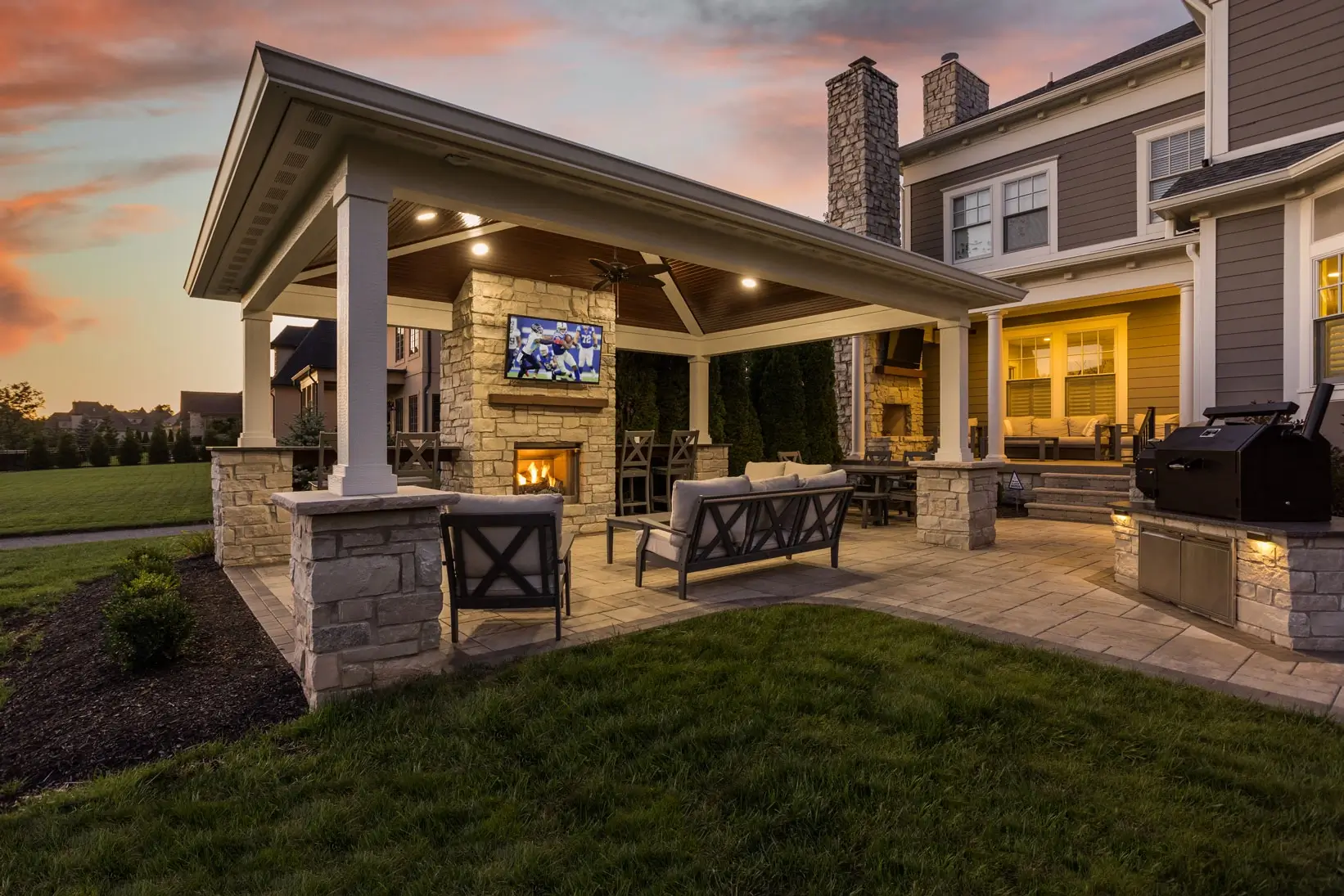 BPI outdoor living space with TV and cozy fireplace with sunset in background